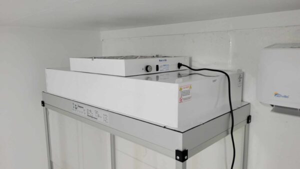 A small room with a Vertical Flow Cabinet 2x4 ft Flowhood Fan Filter Unit New 120V *Freight Not Included*, equipped with a refrigerator on top of it.