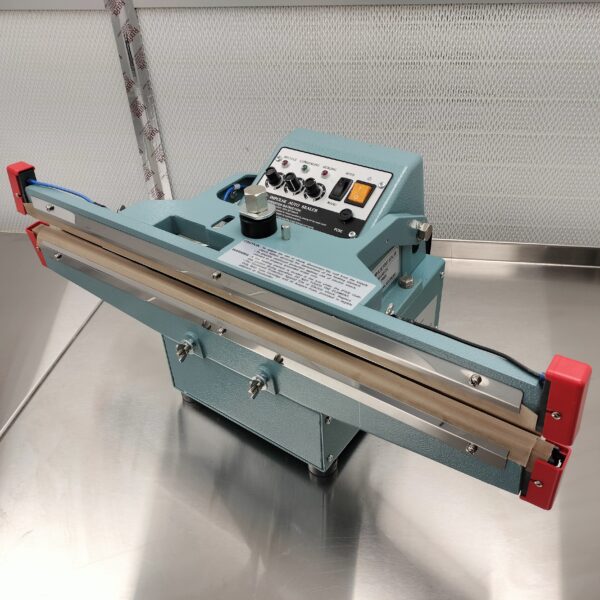 The 24" 10mm Impulse Sealer Dual Element Pedal Operated and Optional Stand is sitting on a metal table.
