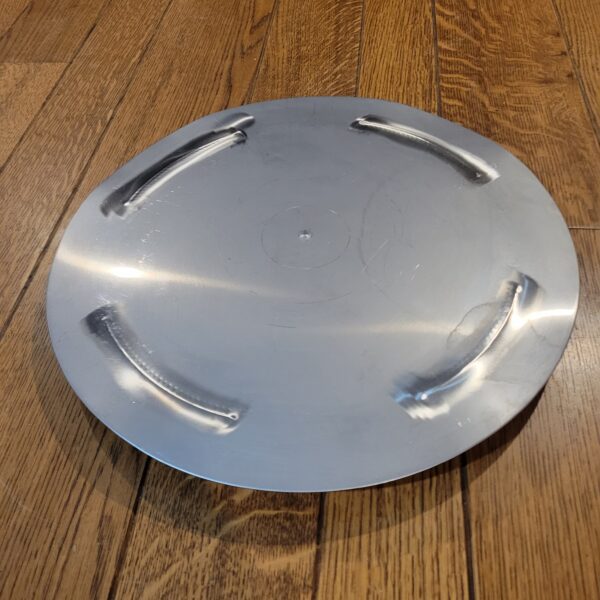 A round metal plate sitting on a wooden floor.
