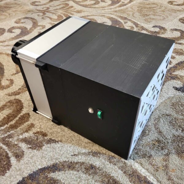 A small, black 10"x10" HEPA Module 120v with a ventilation side grid and a single switch on the front, placed on a patterned carpet.