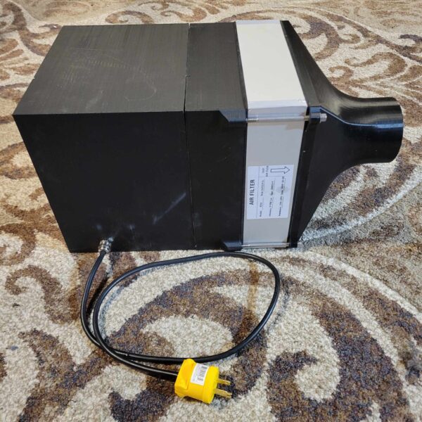 A 10"x10" HEPA Module 120v with a side label and an attached power cord with a yellow plug, resting on a patterned carpet.